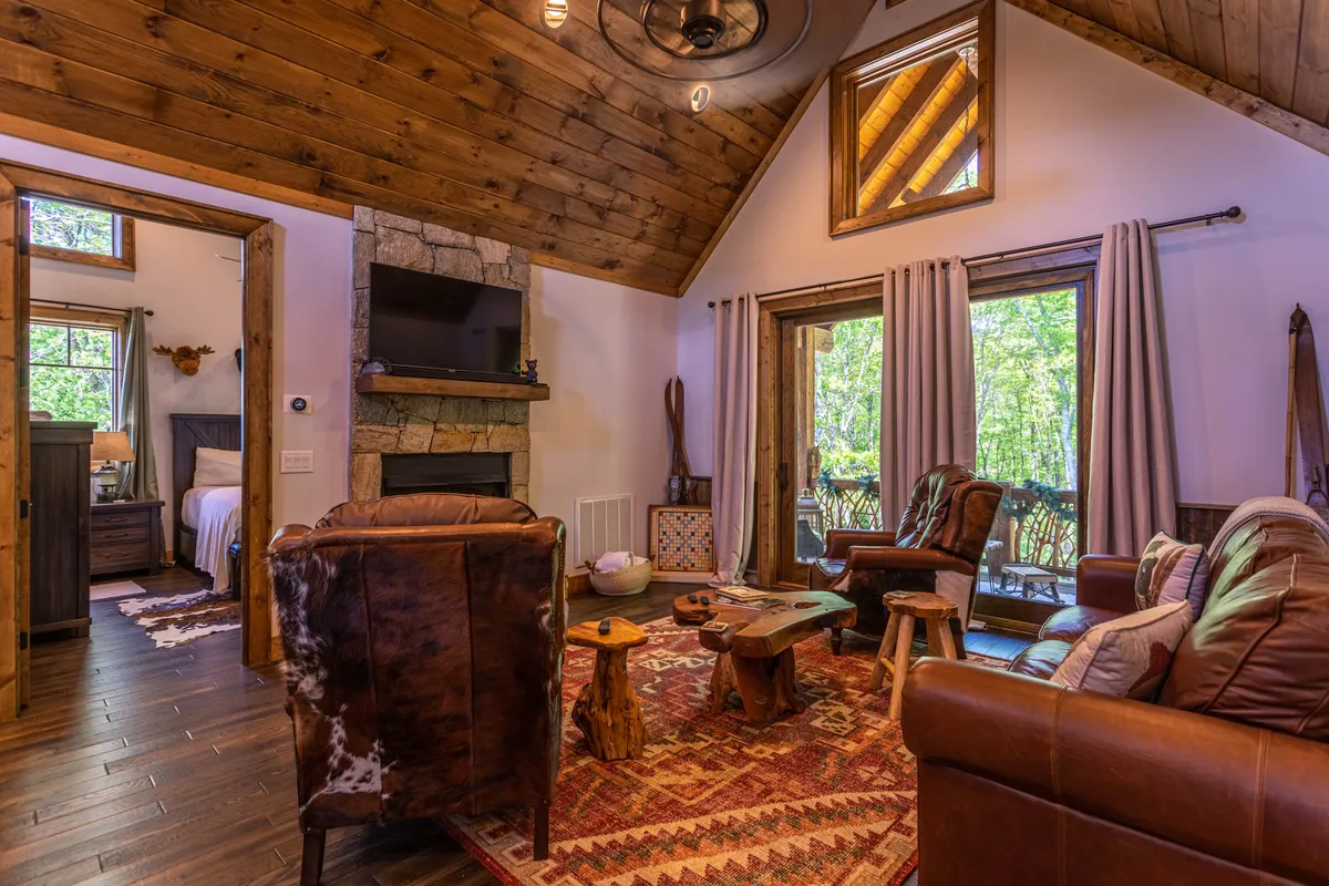 A warm and spacious living space with a fireplace, natural wood furniture, large windows bringing in ample light, and a rustic dining area. The room offers views of the outdoors, reinforcing the connection between the lodge’s interior and the surrounding amenities.