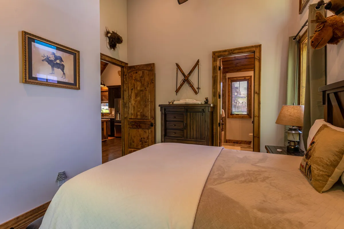 A second inviting bedroom scene with a bed adorned with decorative pillows, a wooden dresser, and rustic décor including framed artwork and antique wooden skis. The room is suffused with a soft, welcoming light, enhancing the sense of warmth and togetherness.