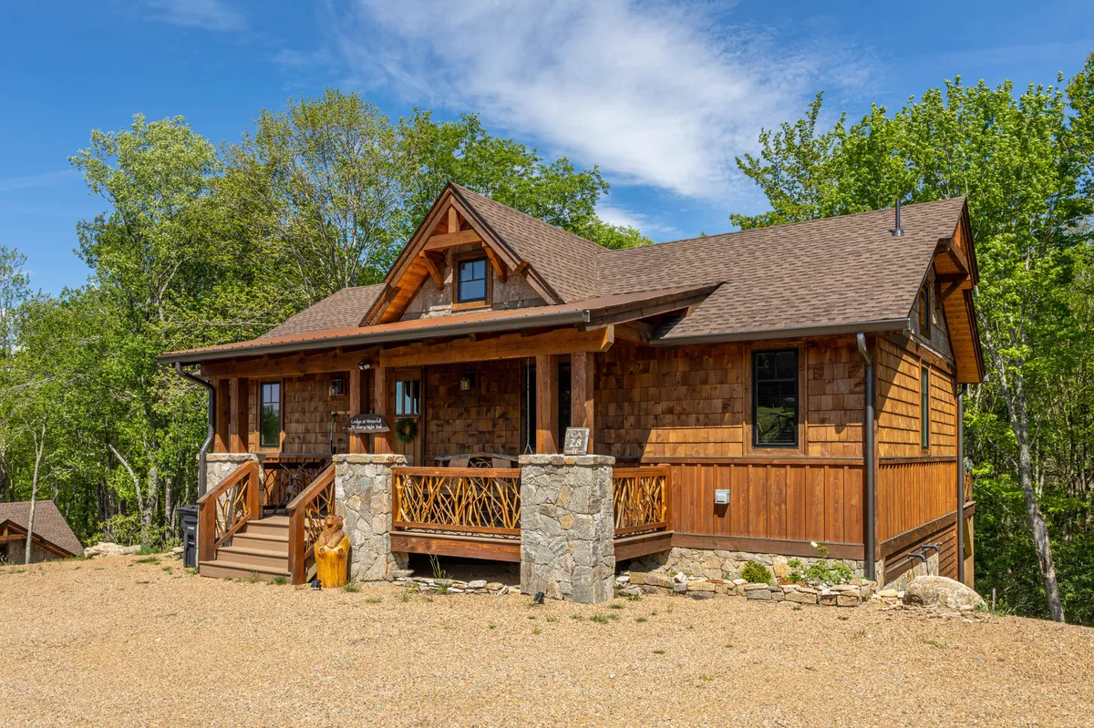 This image captures the inviting exterior of Winterfell Lodge, featuring rustic wooden steps, a sturdy stone facade, and a welcoming front porch with decorative railings. Surrounded by lush greenery and mature trees, the scene radiates a cozy, nature-immersed atmosphere, perfectly illustrating the lodge’s proximity to the outdoors and creekside setting.
